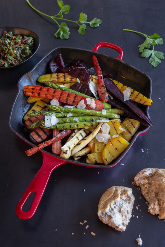 Rode gietijzeren grillpan gevuld met gegrilde groenten, zoals wortelen, asperges en aardappelen.