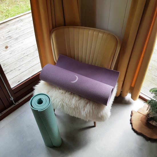 Opgerolde paarse yogamat op een witte vacht, naast een mintgroene mat.