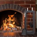 Zwart haardgereedschap naast een brandende bakstenen open haard.