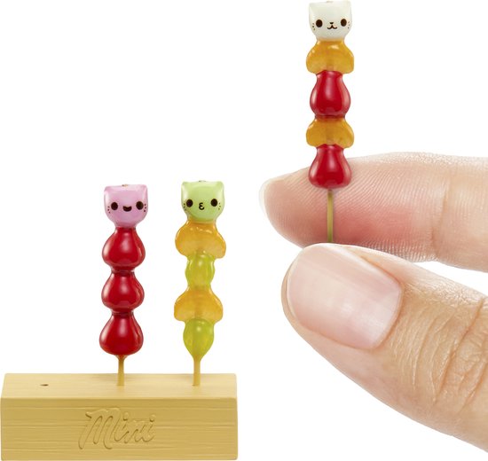 Hand met miniatuur spiesjes met fruit en katten-vormige snoepjes op een houten display.