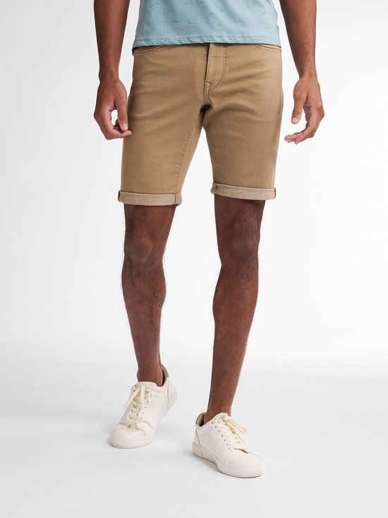 Man in lichtbruine slim fit spijkerbroek, omgeslagen broekspijpen en witte sneakers.