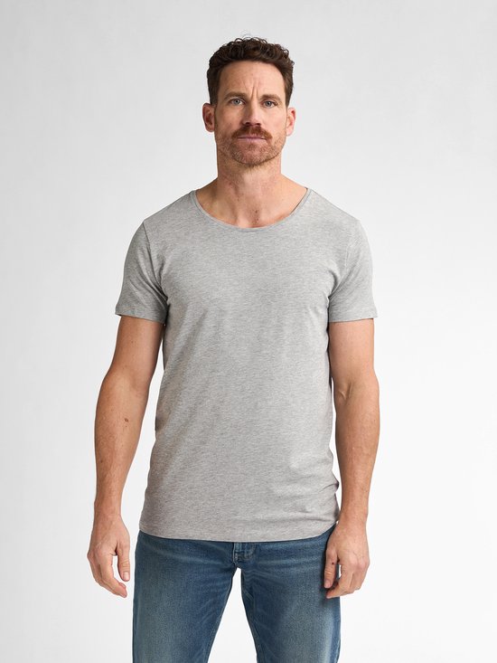 Man met grijze T-shirt met ronde hals en blauwe jeans, staand.