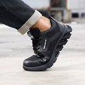 Zwarte werksneaker met robuuste zool, getoond aan een voet in een spijkerbroek.