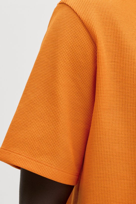 Close-up van de mouw en textuur van een oranje wafel t-shirt.