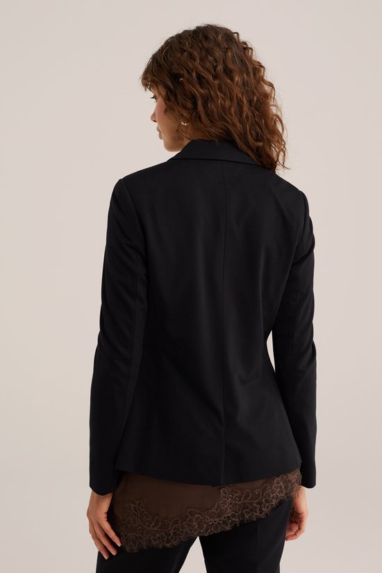 Zijaanzicht van een model met zwarte blazer en bruine kanten top.