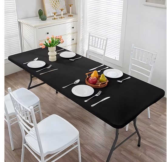 Zwarte klaptafel gedekt met borden, bestek en een mand met fruit in een eetkamer.