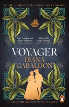 Boek 'Voyager' van Diana Gabaldon. Gouden silhouet van een koppel, omringd door groene bladeren en paarse bessen. Bovenin een zeilschip. 50 miljoen exemplaren wereldwijd verkocht.