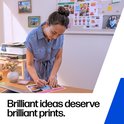 Een vrouw werkt aan een bureau en schrijft op een geprint document. Tekst: "Brilliant ideas deserve brilliant prints."