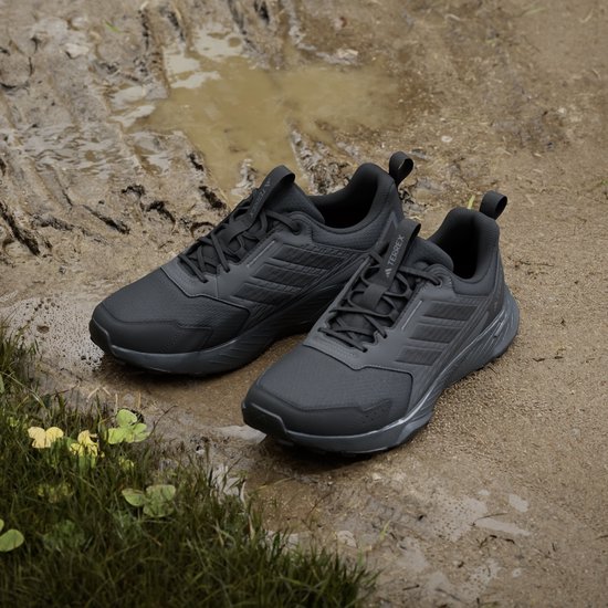 Paar zwarte Adidas Terrex trailrunningschoenen in de modder, met gras op de voorgrond.