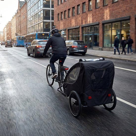 Man op fiets met zwarte fietskar met kinderen door stad.
