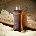 Bruine fles Hawaiian Tropic Glowing Oil Tanning Oil op een rotsachtige ondergrond, met capsule met vitamine E.