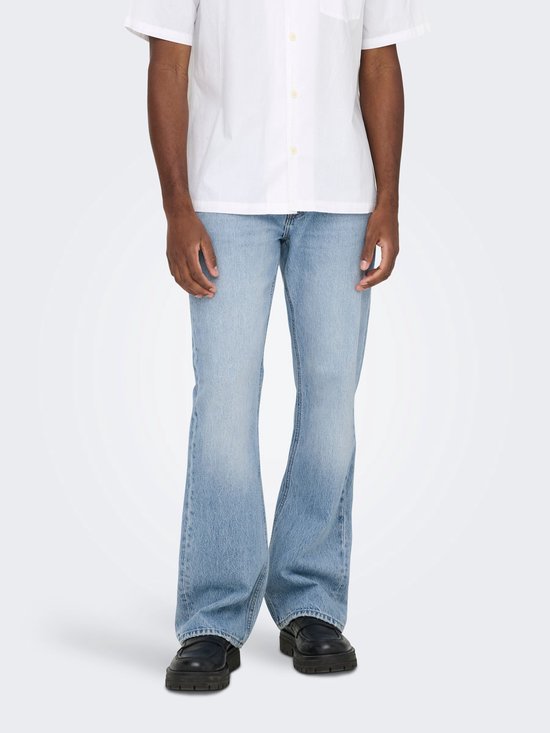 Man van voren in witte korte mouwen blouse en lichtblauwe flared jeans, met zwarte loafers.