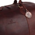 Detail van bruine leren reistas met 'DE LAMASSU'-logo en koperkleurige hanger.
