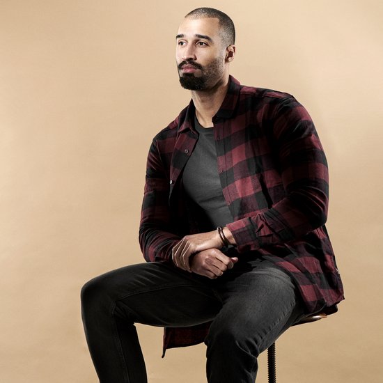 Man met donker haar en baard, zittend, met een rood-zwart geruite blouse aan.