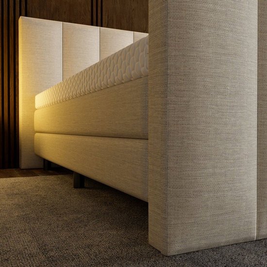 Zijaanzicht van de beige boxspring met gestreept hoofdbord en matras met honingraatpatroon.