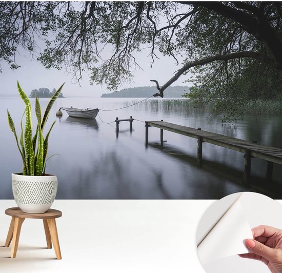 Un lac calme avec un petit bateau et un quai en bois, entouré de branches d'arbres luxuriantes et de roseaux.