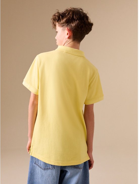 Jongen met krullend haar draagt een lichtgeel poloshirt met korte mouwen, gezien vanaf de achterkant.