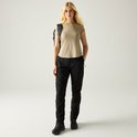 Dames in een zwarte outdoorbroek, beige t-shirt en rugzak, van voren gezien.