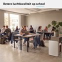 Witte luchtreiniger in een klaslokaal met leerlingen aan tafels.