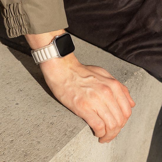 Hand van een persoon met een zilverkleurig horloge met lichtbeige stoffen bandje, rustend op een betonnen rand.