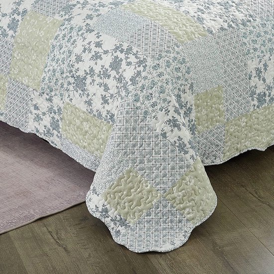 Hoek van een bed met een blauwgroene patchwork quilt met bloemenprints en ruitpatronen.