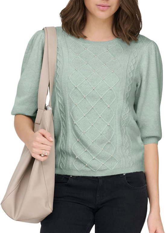 Pull vert pâle orné de perles et d'un motif torsadé. Manches bouffantes trois-quarts. Le mannequin porte un pantalon noir et un sac beige.