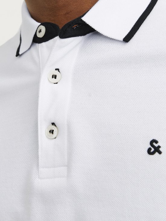 Detail van een wit poloshirt met zwarte kraagbies, knopen en logo.