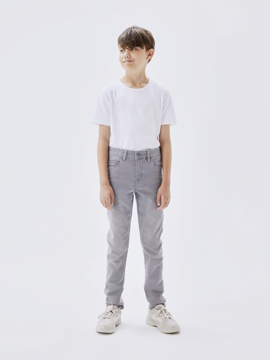 Jongetje in een witte T-shirt en strakke, grijze jeans.