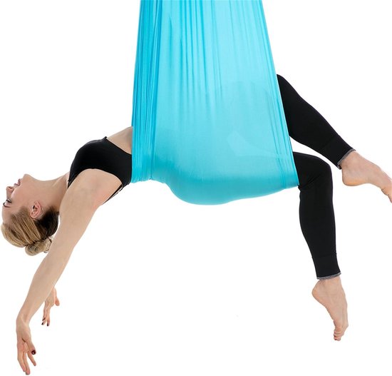 Vrouw hangt achterover in een blauw yogadoek, benen naar achteren gebogen.