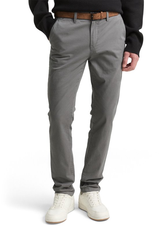 Man met grijze chino broek, bruine riem, zwart trui en witte sneakers.