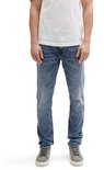 Man in wit T-shirt en slanke, lichtblauwe spijkerbroek.