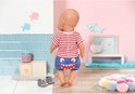 Baby Born pop staand, met rood-wit gestreept shirt met haai en blauwe broek met haaientanden. Draagt grijze haaienschoentjes.