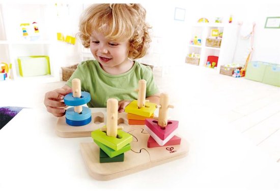 Een jong kind met krullend blond haar speelt met de Hape Steckpuzzle met blauwe, groene, gele en roze vormpjes.