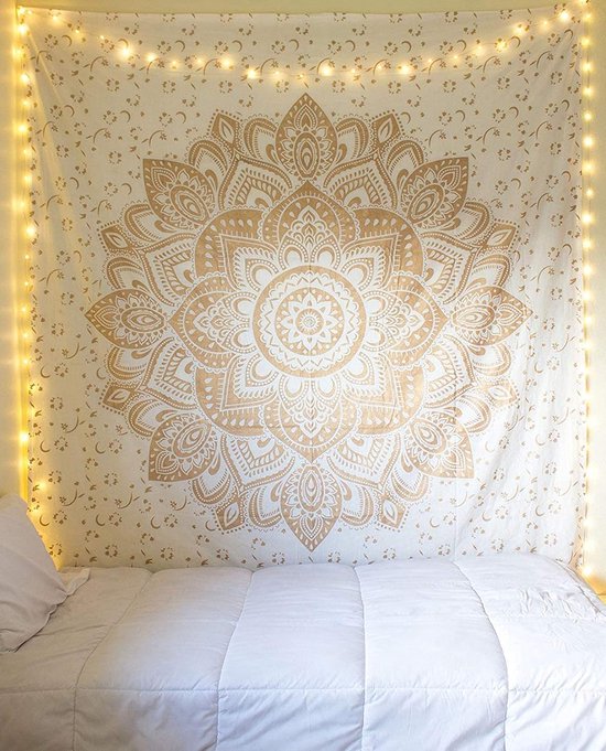 Gouden mandala wandkleed met kleine bloemetjes, hangend boven een opgemaakt bed met kerstverlichting.