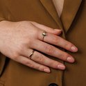 Gouden ring met smalle band en ovaal groene steen, gedragen op modelhand.