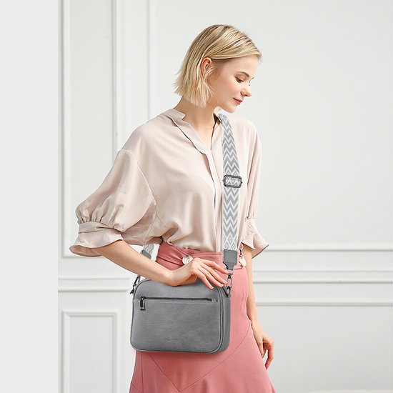 Grijze veganistische leren crossbody tas gedragen door een vrouw met een chevron patroon band.