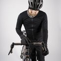 Een man met een zwarte fietsoutfit, helm en nekwarmer, leunt over een racefiets met grijze stuurlint. Hij draagt ook zwarte handschoenen.