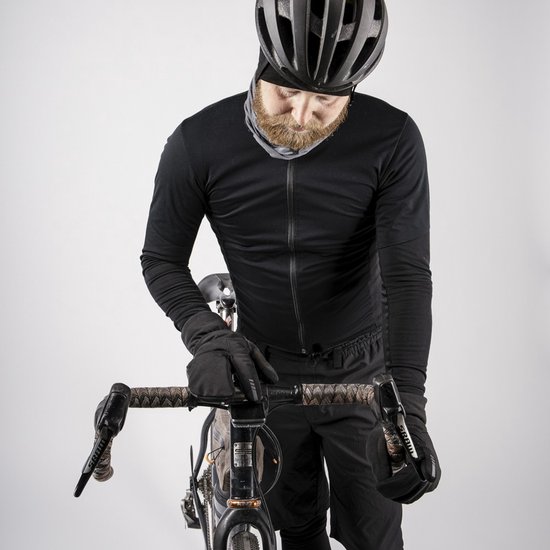 Een man met een zwarte fietsoutfit, helm en nekwarmer, leunt over een racefiets met grijze stuurlint. Hij draagt ook zwarte handschoenen.