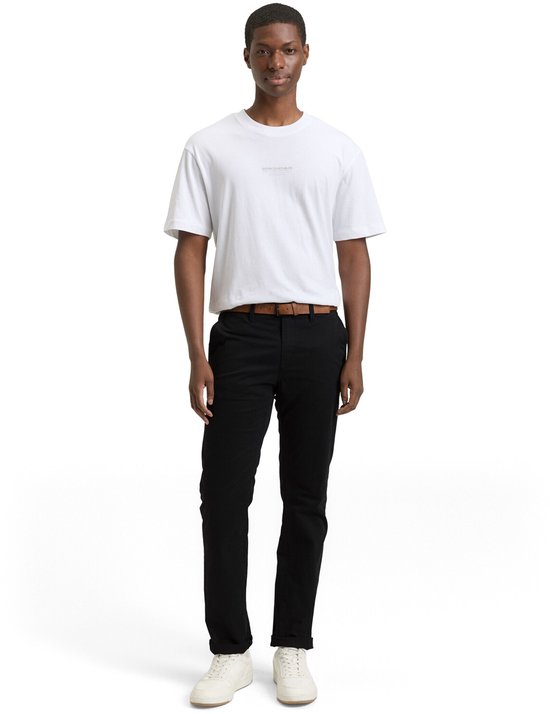 Man in zwarte chino met bruine riem en witte T-shirt en sneakers.