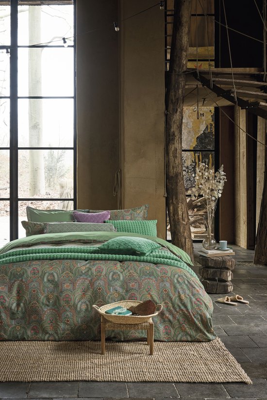 Slaapkamer met een groen bed, gedrapeerd met kussens en een dekbedovertrek met paisley print.