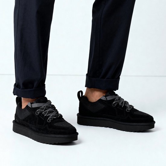 Voeten in donkere broeken en zwarte UGG LO Lowmel sneakers met dikke zolen.