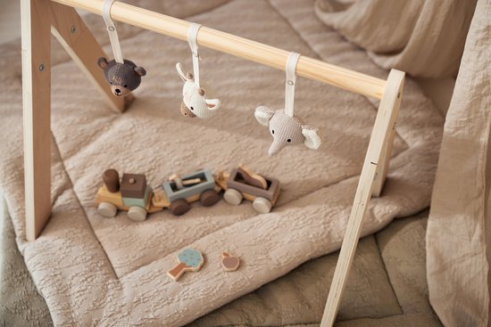 Houten babygym met beige speelmat met trein en houten speeltjes, met hangende knuffels van een beer, muis en olifant.
