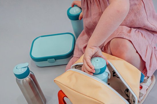 Un enfant en robe rose met une tasse à boisson bleu clair dans un sac jaune.