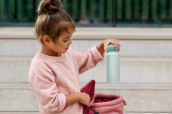 Fille en pull rose attrapant une gourde vert menthe dans un sac rose pâle.