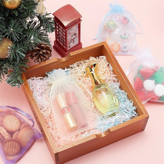 Een houten kistje met crêpepapier, gevuld met een parfumflesje en twee lippenstiften, naast een kerstboom en snoepjes in organzazakjes.