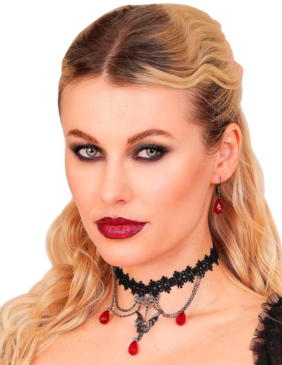 Model met golvend blond haar, draagt een zwarte kanten choker met vleermuis en rode druppels en oorbel.