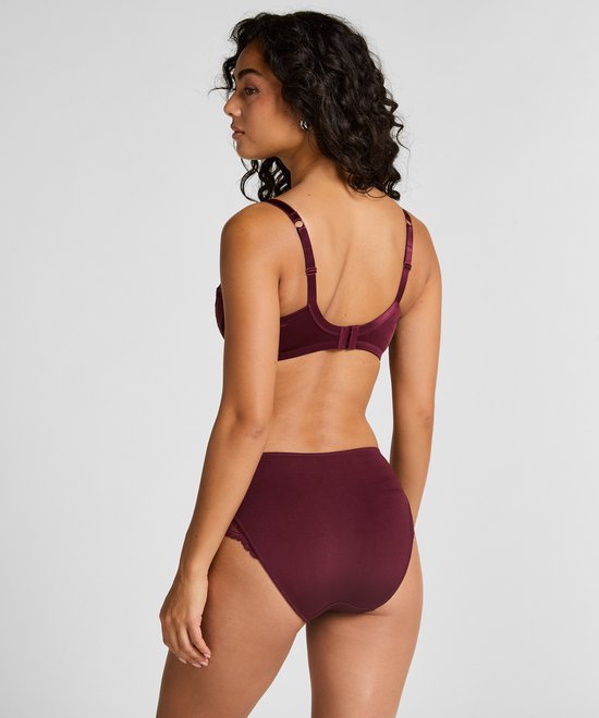 Vrouw draagt bordeauxrode bh met stipjes en kanten details en bijpassende broek.