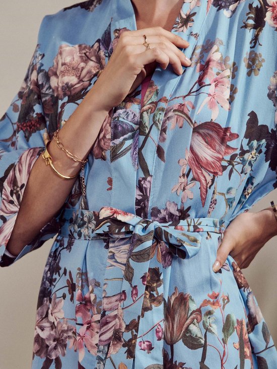 Close-up van een blauwe kimono met een levendige bloemenprint, strik in de taille en gouden armband.