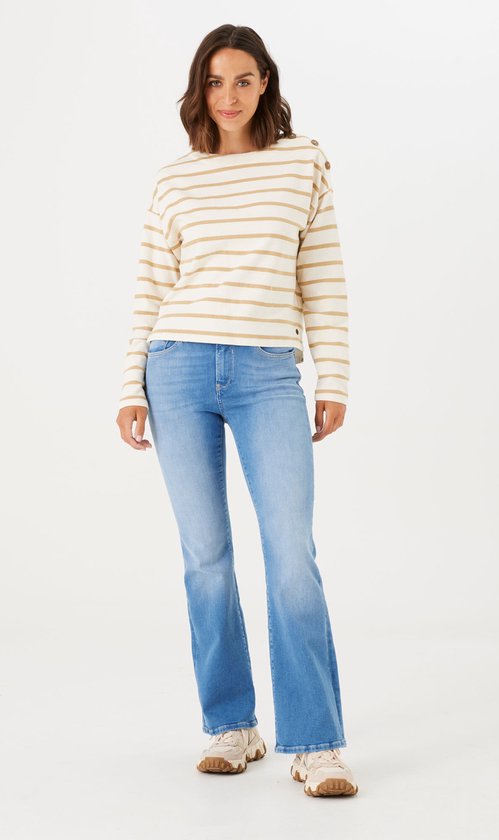 Model draagt een gestreepte trui en blauwe flared jeans met beige sneakers.