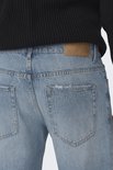 Close-up van de achterkant van een lichtblauwe jeans met distressed achterzakken en een bruin merklabel.